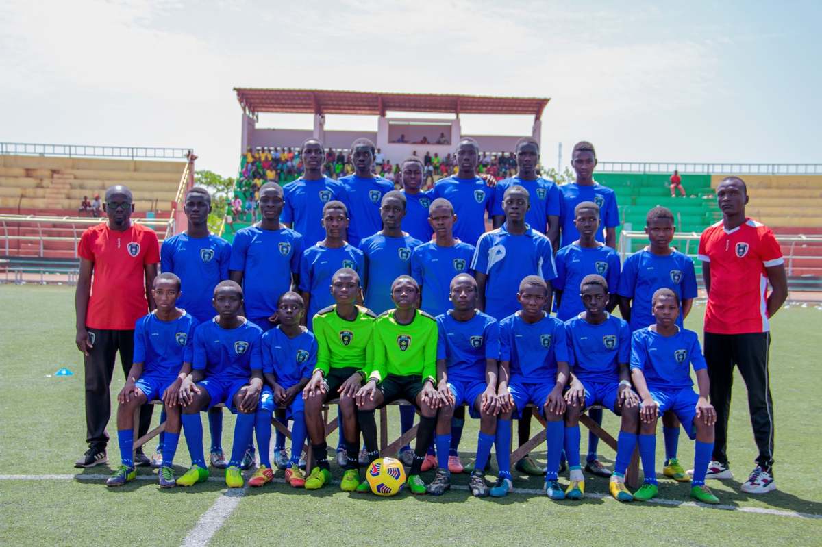 La photo officielle de l'équipe garçons de Hooli Académie en maillot bleu, avec deux encadrants, au stade.